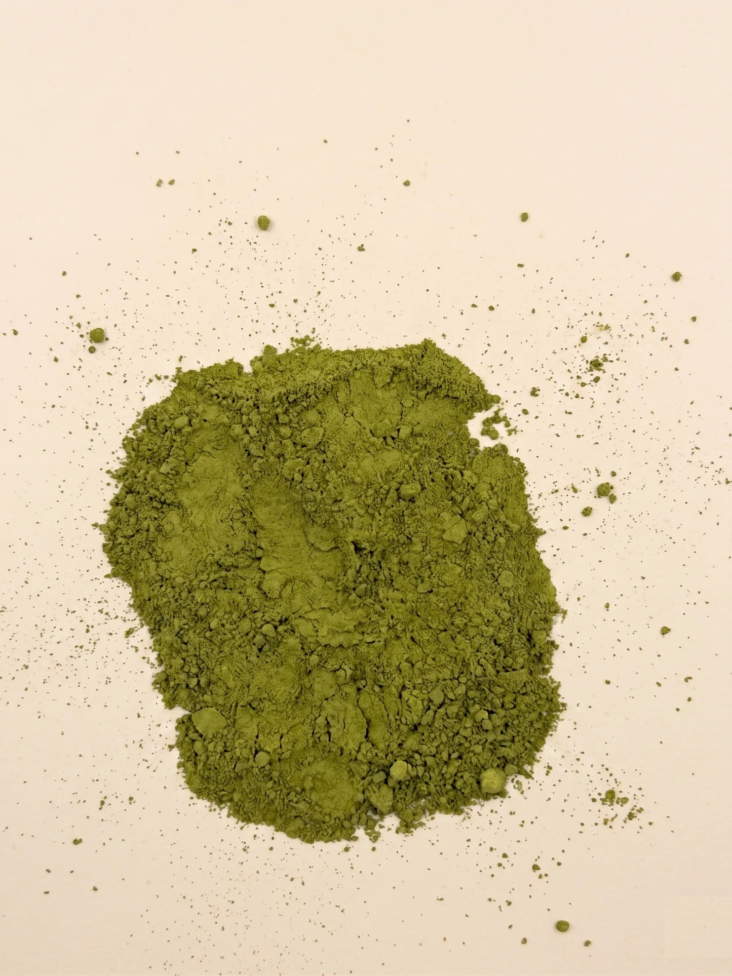 A pile of finely ground, vibrant green Catawba Yaupon matcha style tea powder on a light cream background.