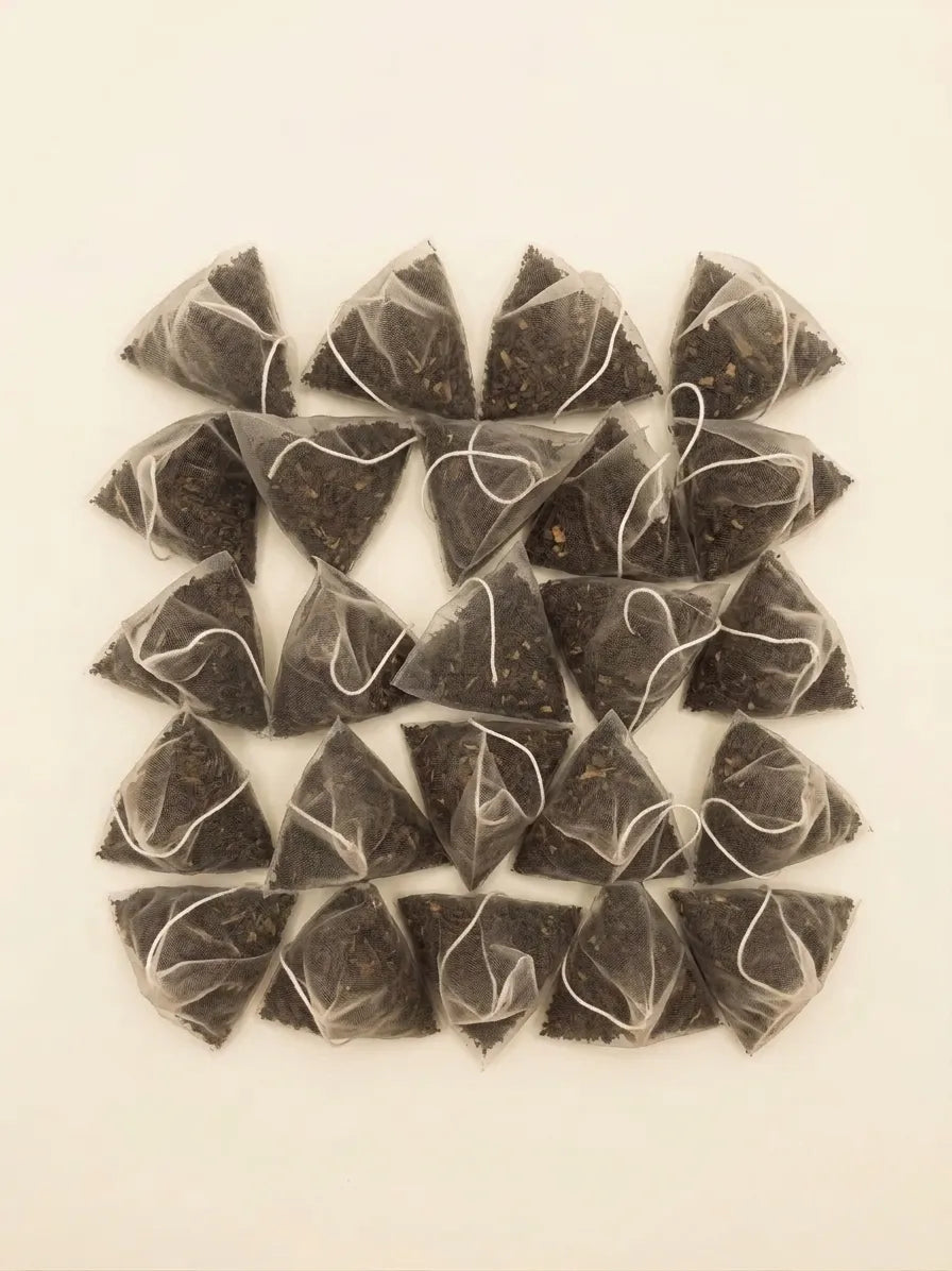 A top-down view of pyramid mesh tea sachets filled with loose roasted yaupon tea leaves arranged in a grid.
