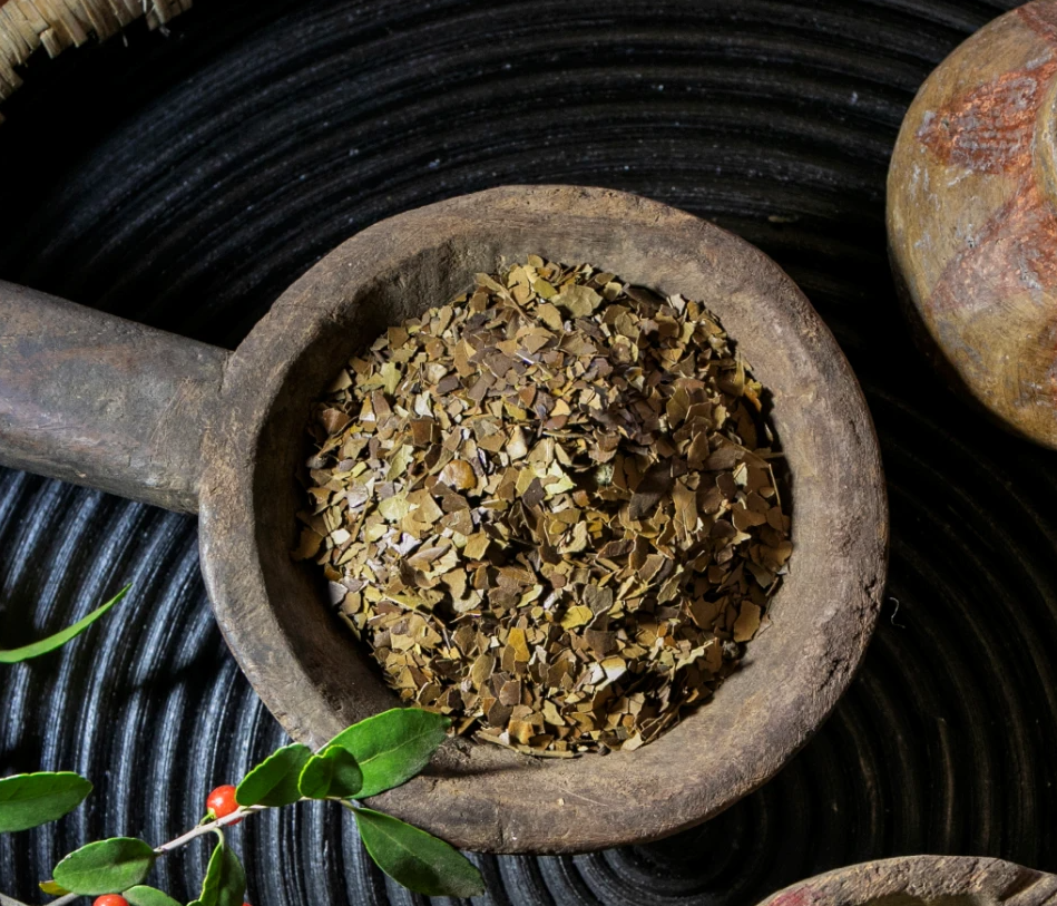 A close-up top-down view of roasted yaupon loose leaf tea inside a rustic wooden scoop, showing the texture of the dried leaves.