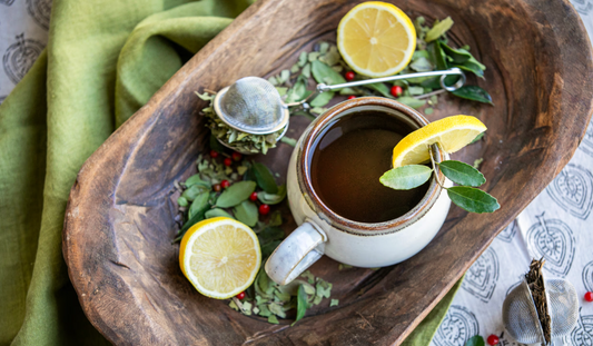 Freshly brewed Yaupon Tea with a metal infuser, loose leaves, and citrus accents on a minimalist table setting.
