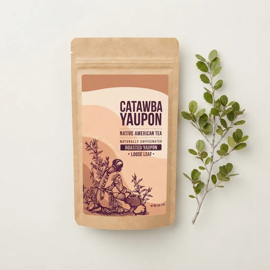 A brown kraft paper pouch of Catawba Yaupon roasted loose-leaf tea, positioned next to a fresh Yaupon holly sprig against a clean, light-colored background.