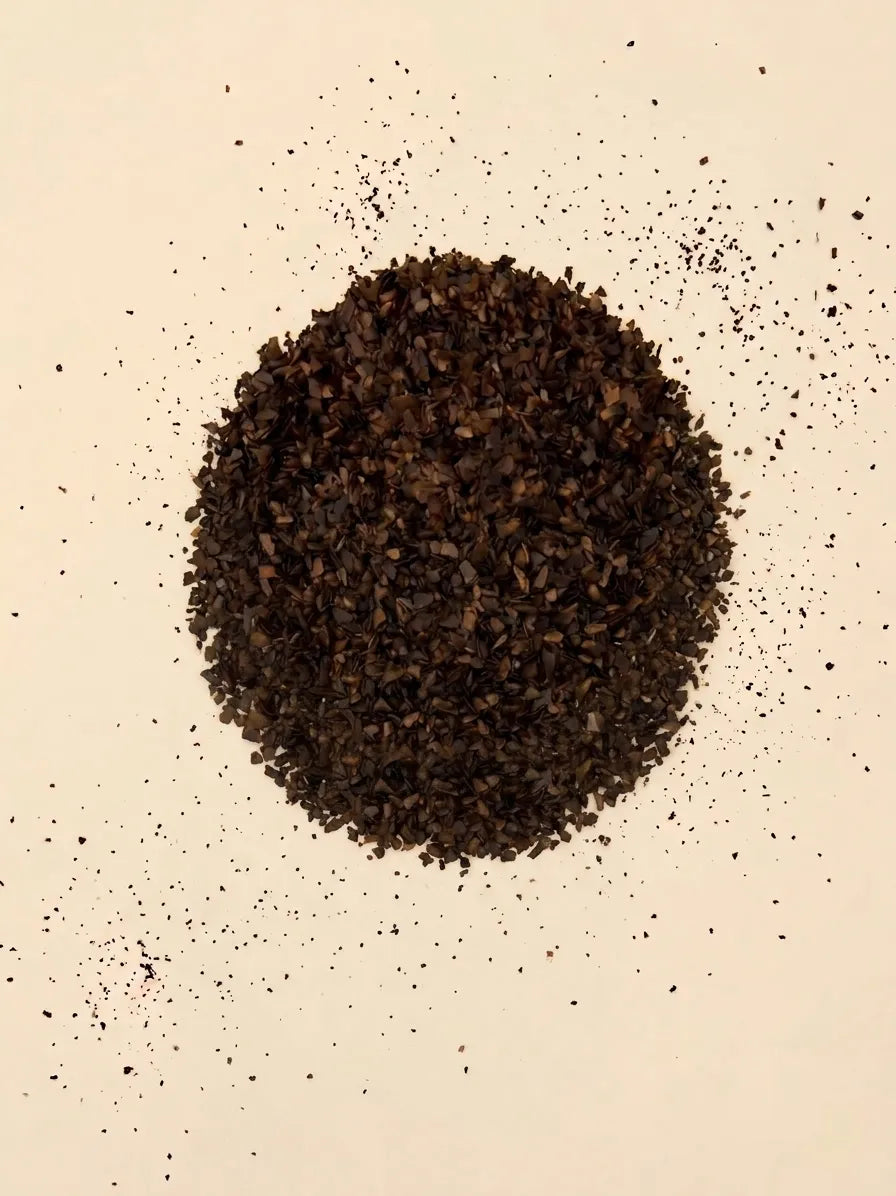 A top-down view of a circular pile of loose cut Catawba Yaupon Black tea leaves on a light cream surface.