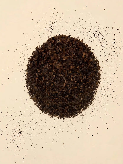 A top-down view of a circular pile of loose cut Catawba Yaupon Black tea leaves on a light cream surface.
