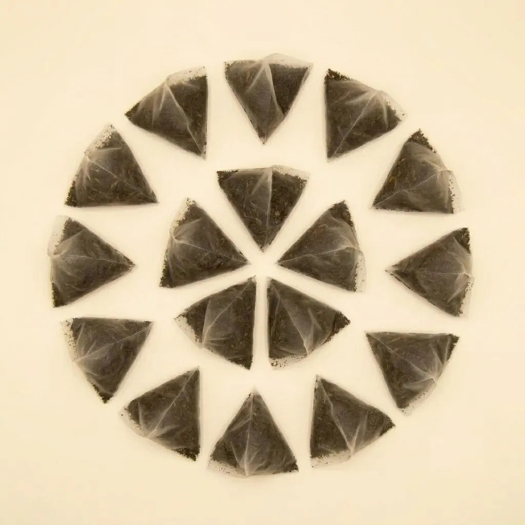 A top-down view of pyramid mesh tea sachets filled with loose black yaupon tea leaves arranged in a circular pattern.