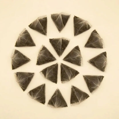 A top-down view of pyramid mesh tea sachets filled with loose black yaupon tea leaves arranged in a circular pattern.
