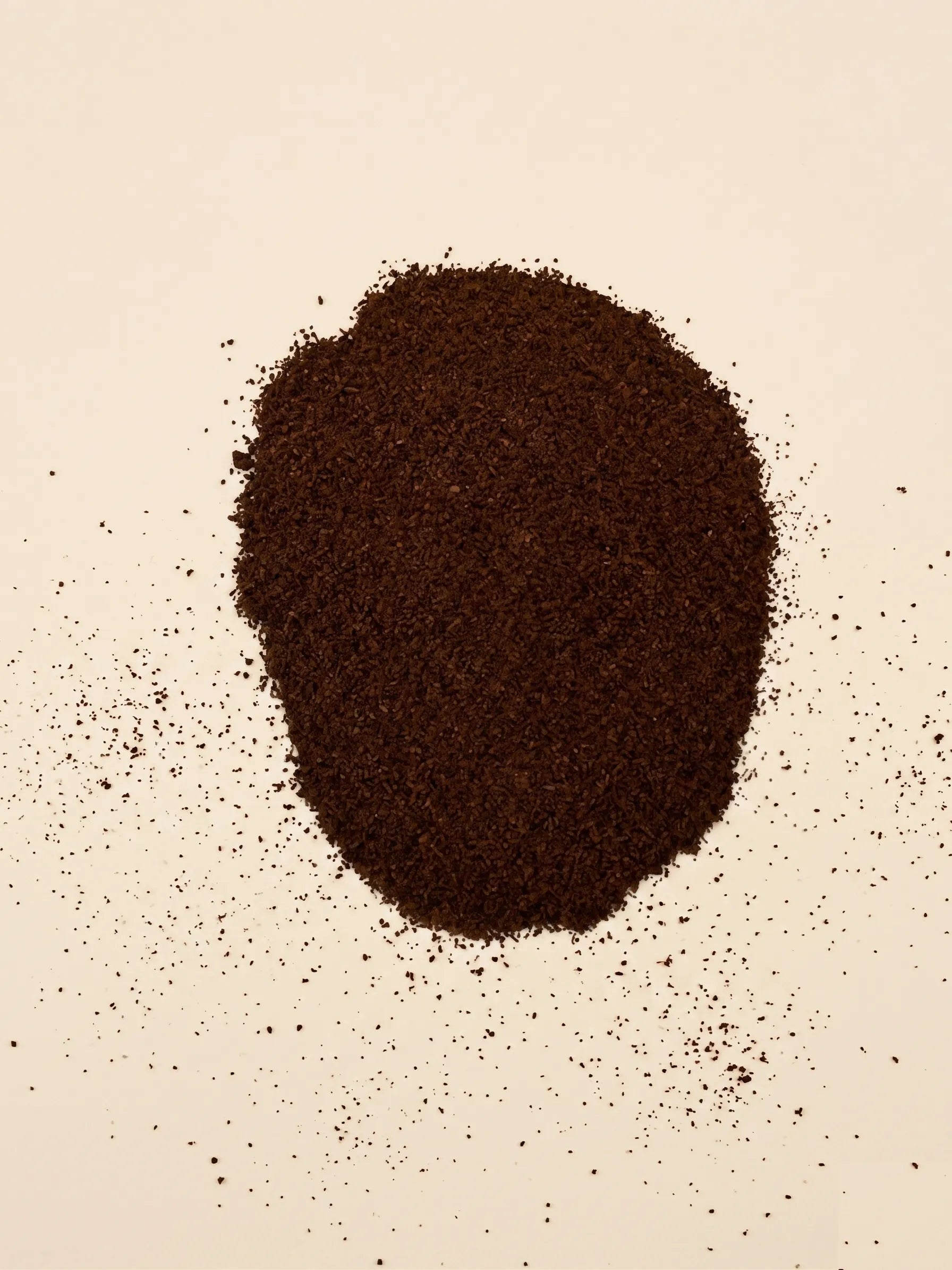 A circular pile of finely ground, dark roast Catawba Yaupon espresso tea on a light cream surface.