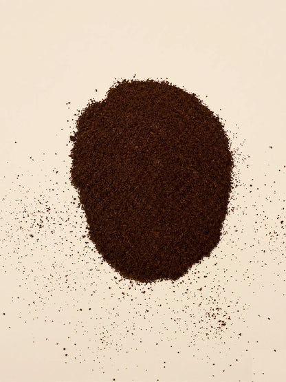 A circular pile of finely ground, dark roast Catawba Yaupon espresso tea on a light cream surface.