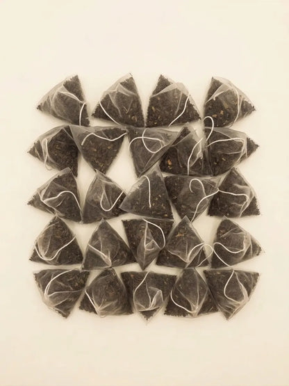A top-down view of pyramid mesh tea sachets filled with loose roasted yaupon tea leaves arranged in a grid.