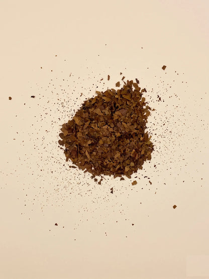 A central pile of crushed brown yaupon loose leaf tea with fine tea dust scattered across a cream background.